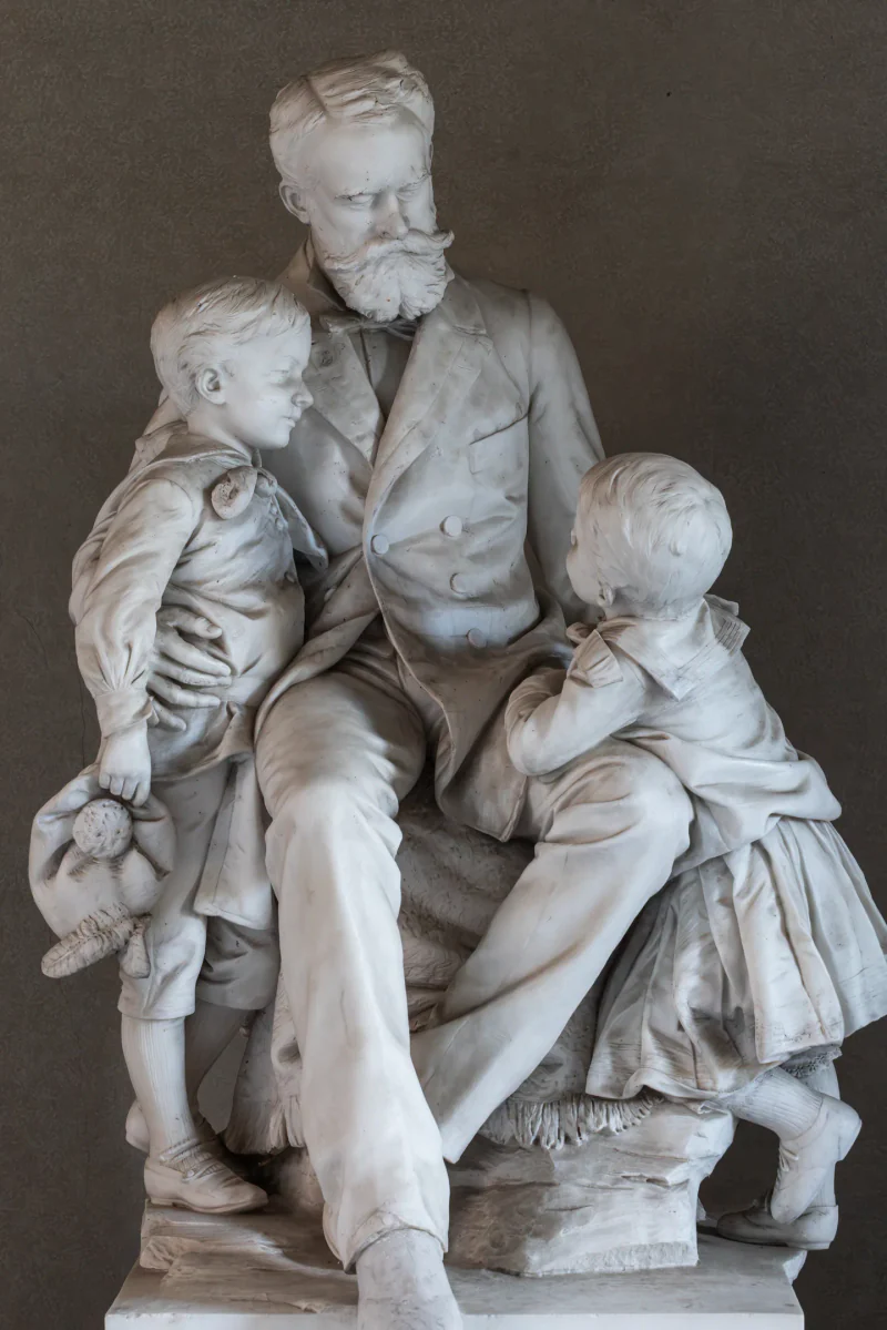 A white sculpture of a seated bearded man with two children at the castle.