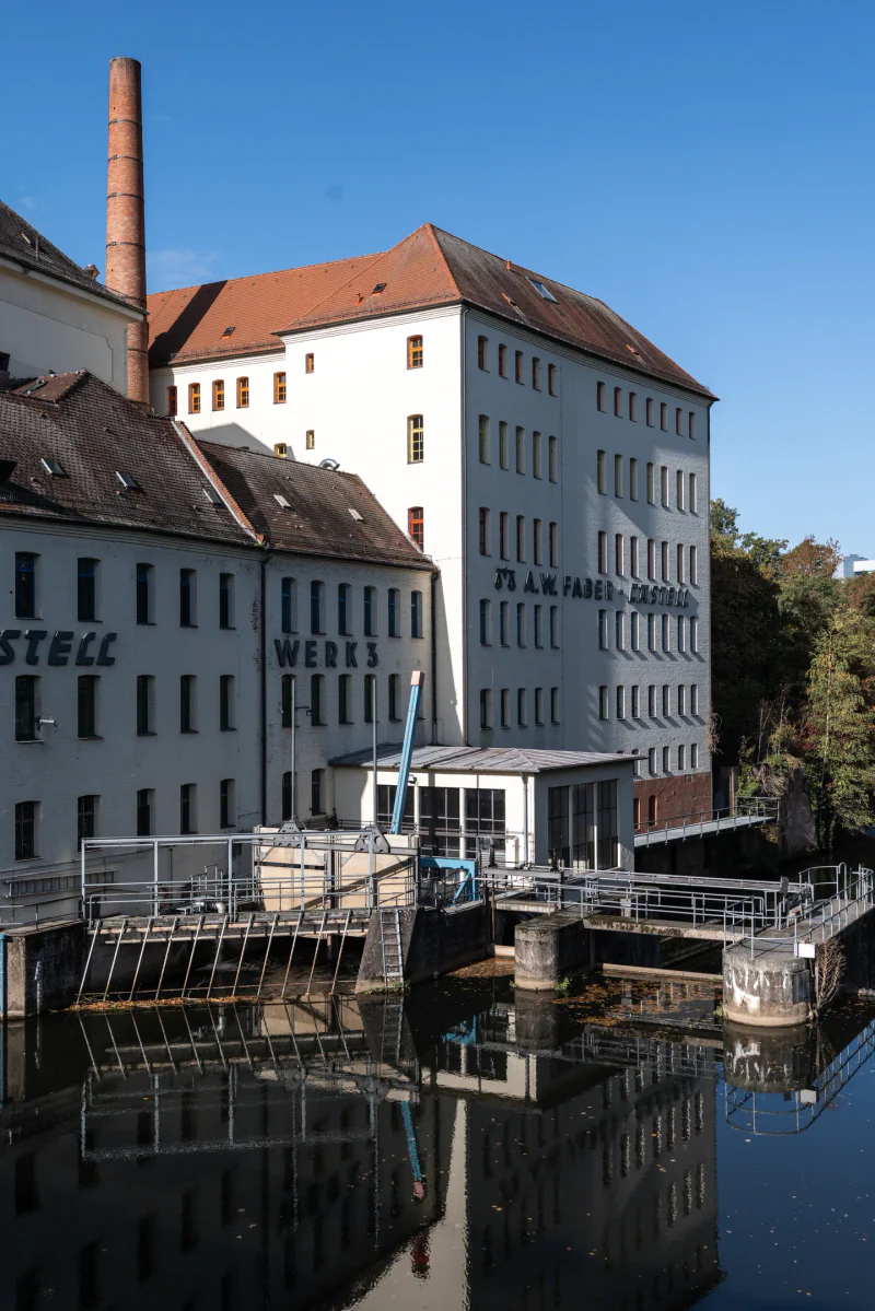 Historic factory buildings and water-control structures reflected in the Rednitz.
