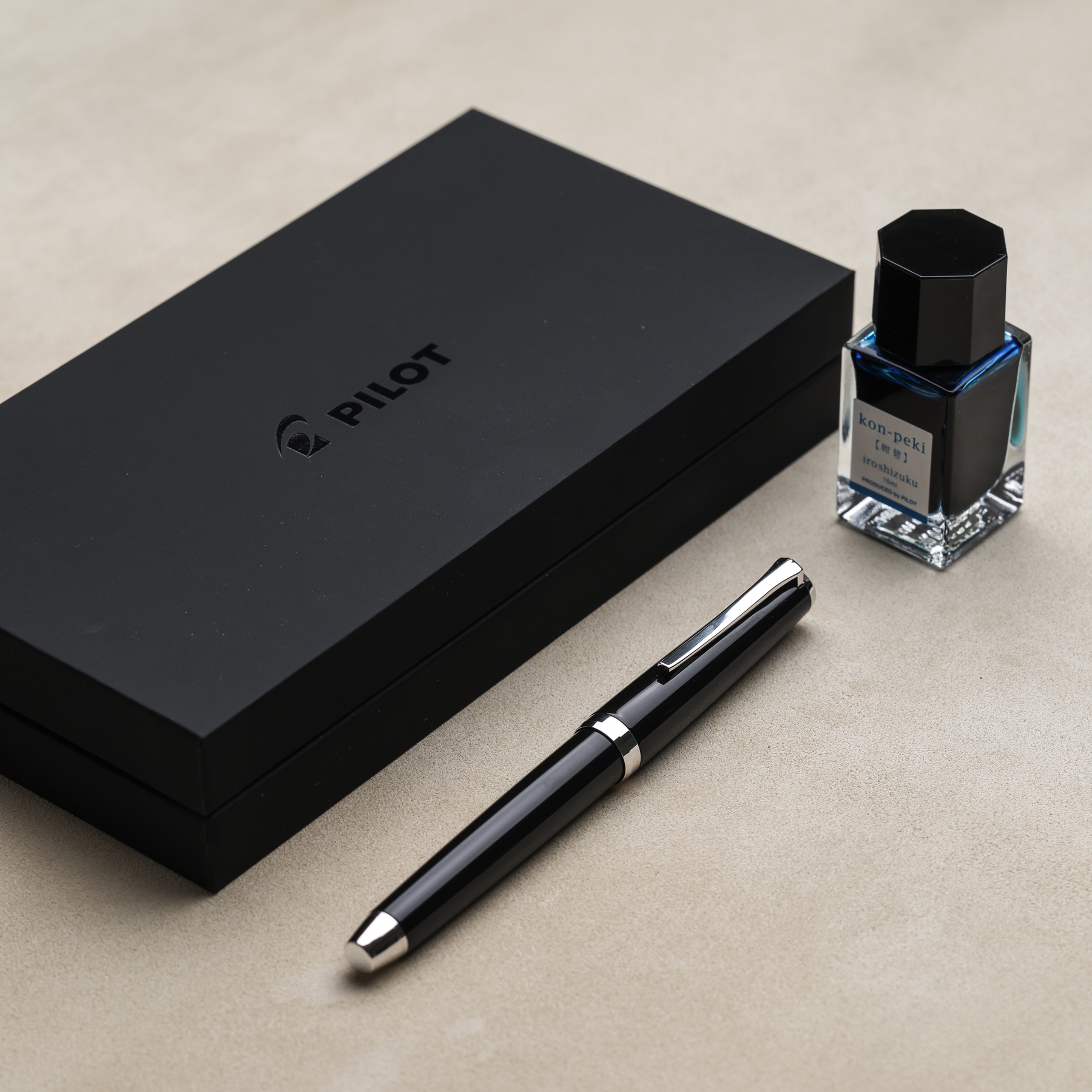 Black resin Pilot Falcon fountain pen beside its presentation box and blue ink