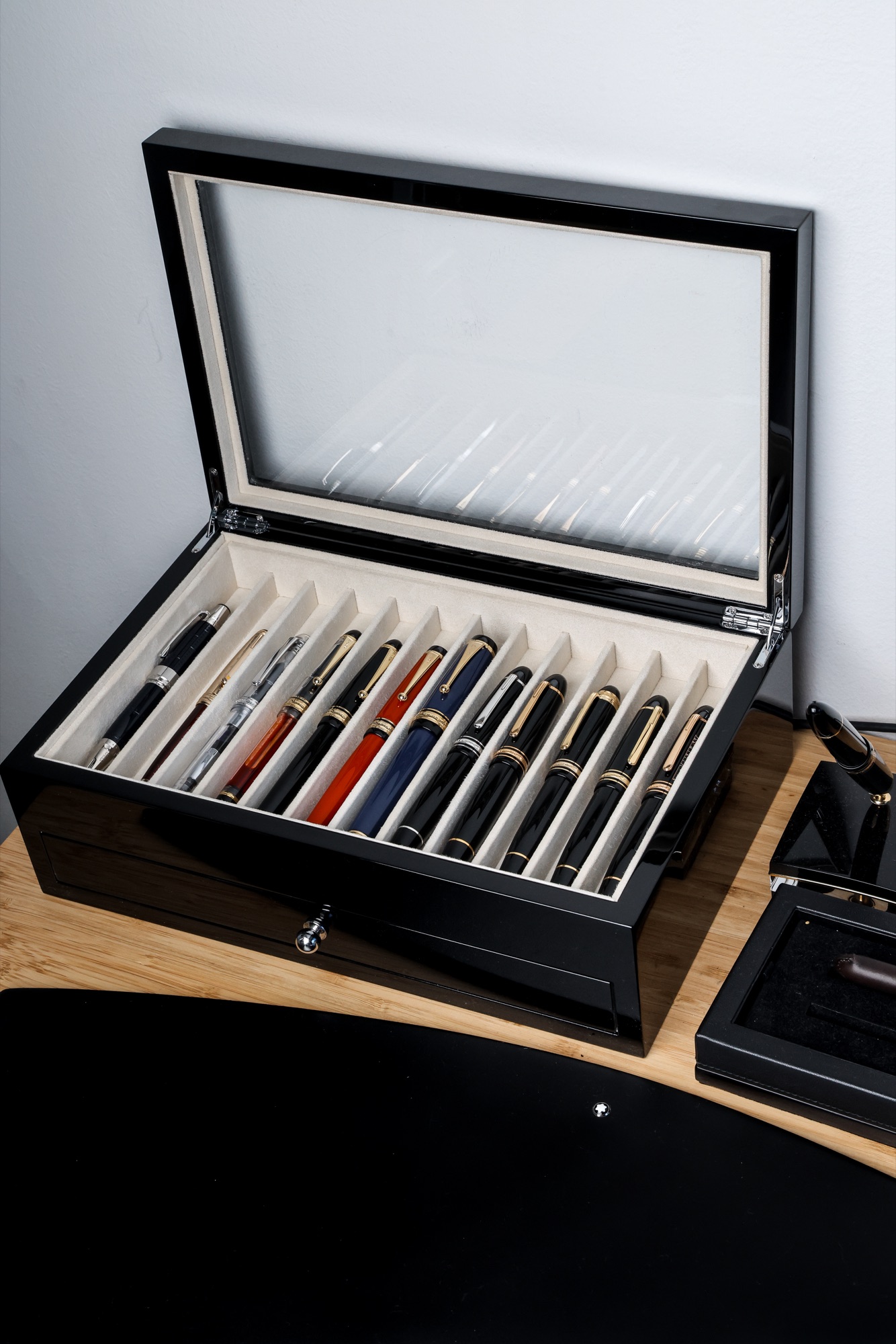 Fountain pens arranged in a cream-lined black display case with an open glass lid