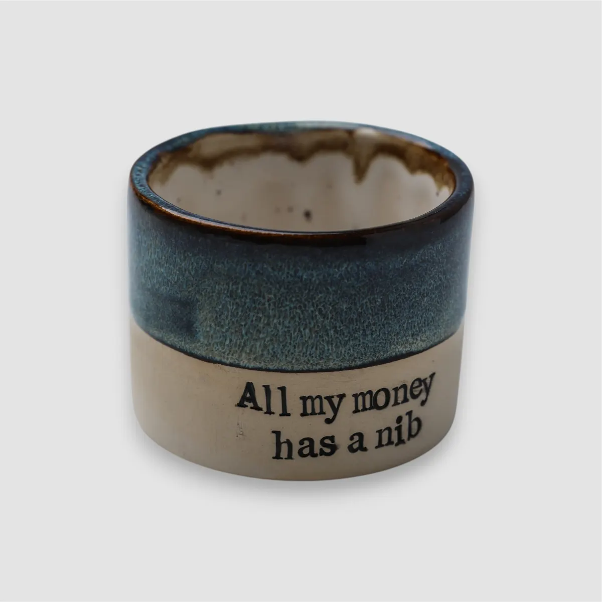 Handmade All My Money Has a Nib ceramic mug by KERANIKA with blue glaze, a natural clay base and black lettering