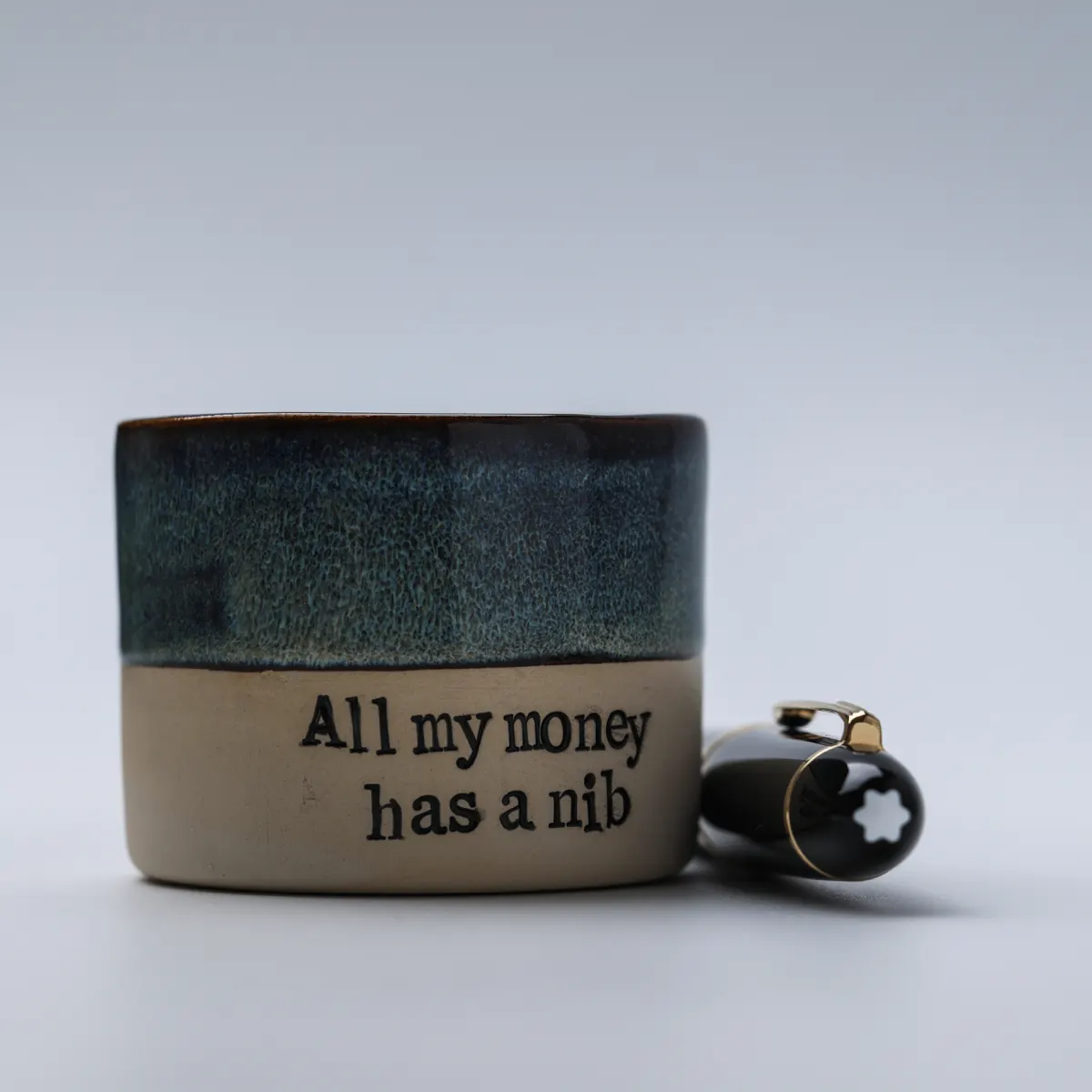 All My Money Has a Nib mug beside a black fountain pen with a white star emblem on its cap