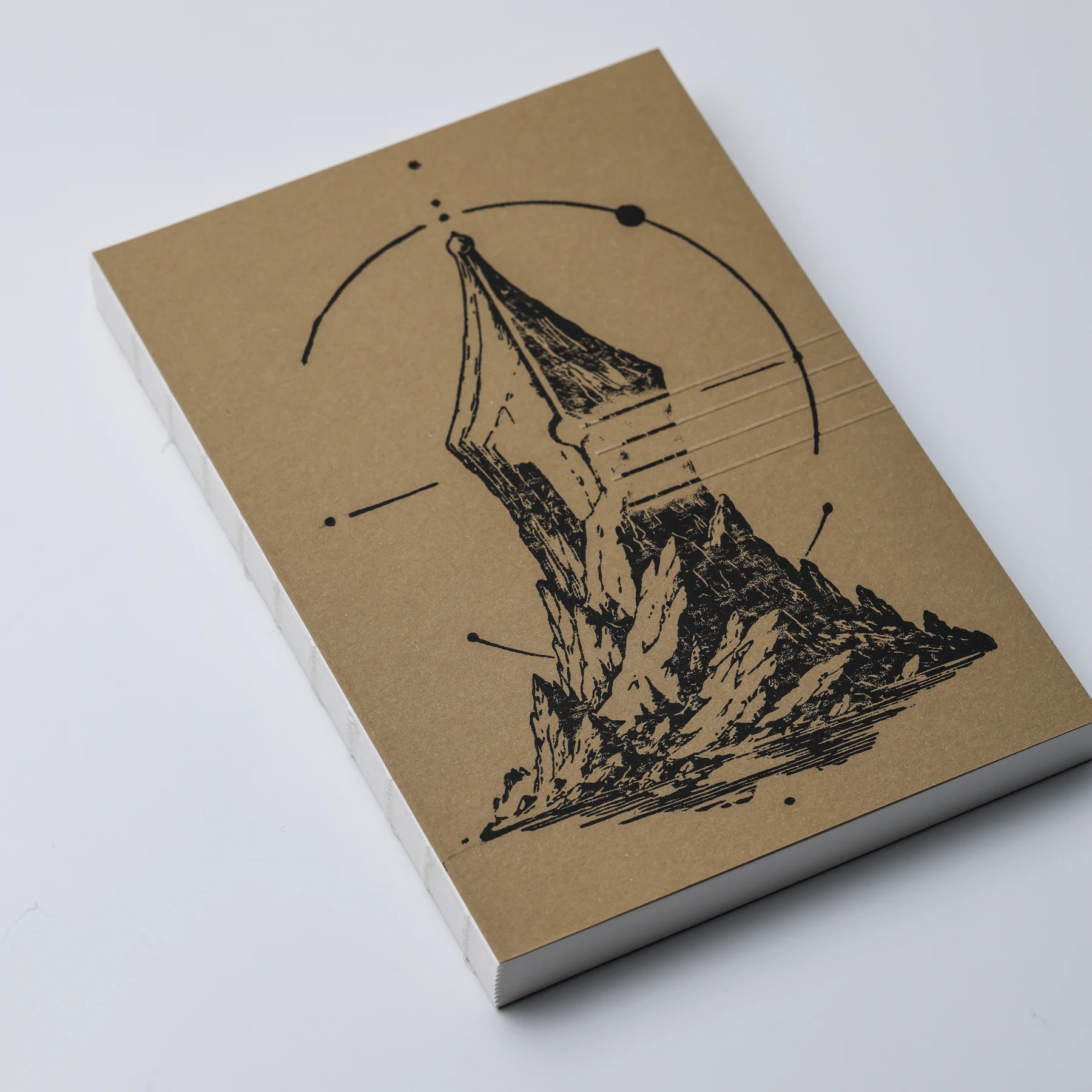 Angled view of the FMP Notebook No.1 ASCENT natural paper cover with a black fountain pen nib and mountain design