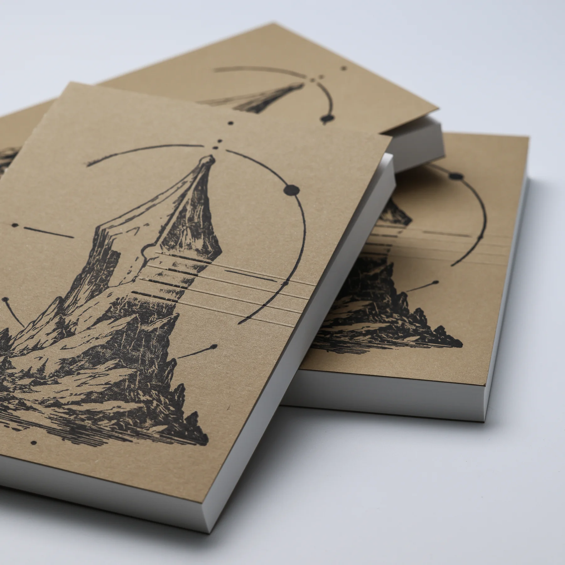 Overlapping ASCENT notebook covers showing the black linocut artwork, embossed lines and thick paper blocks