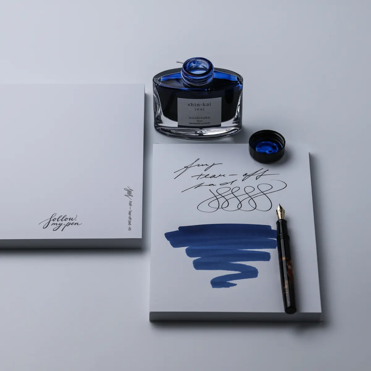 FMP paper with handwriting and blue ink swatches beside an A5 pad, a fountain pen and Shin-kai ink