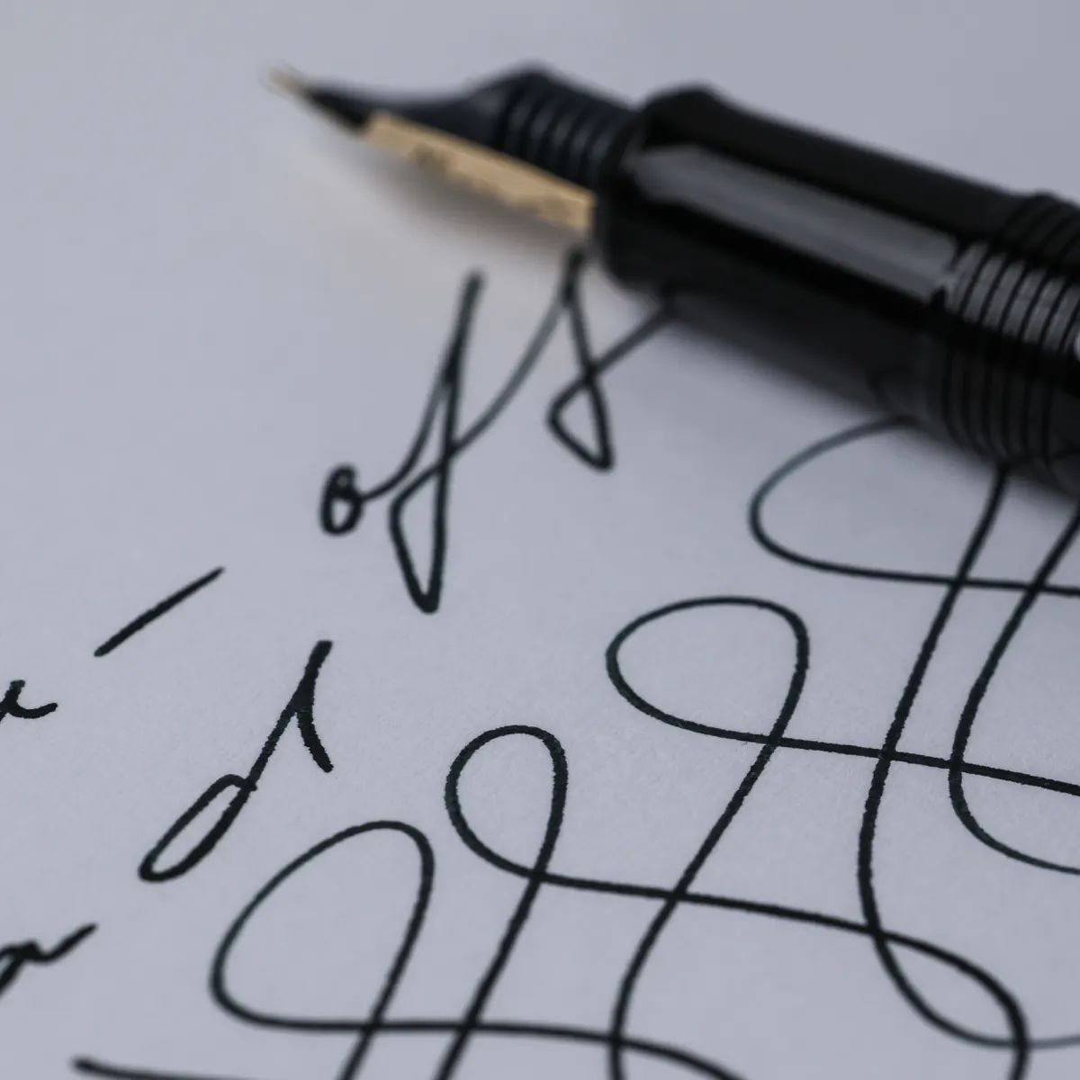 Macro view of handwritten black ink loops on white FMP paper, with a fountain pen across the upper edge