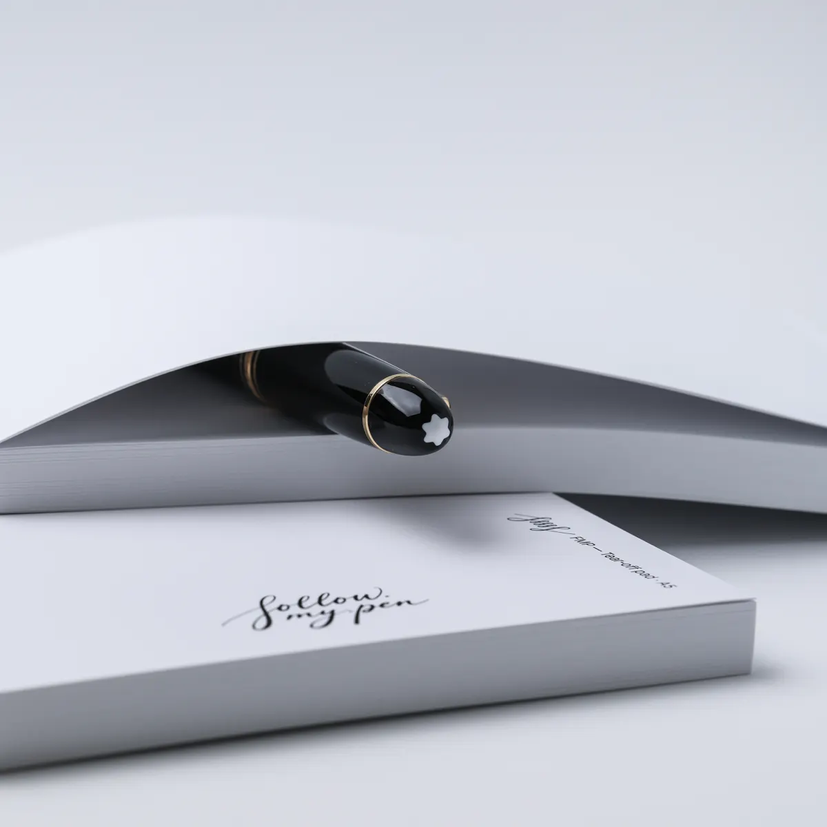 Side view of a lifted white paper sheet with a black fountain pen beneath it and an FMP A5 pad in front