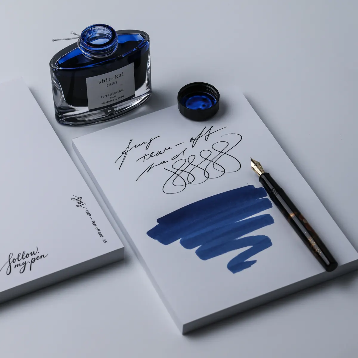 Angled view of handwriting and blue ink swatches on FMP paper with an open Pilot Iroshizuku Shin-kai bottle