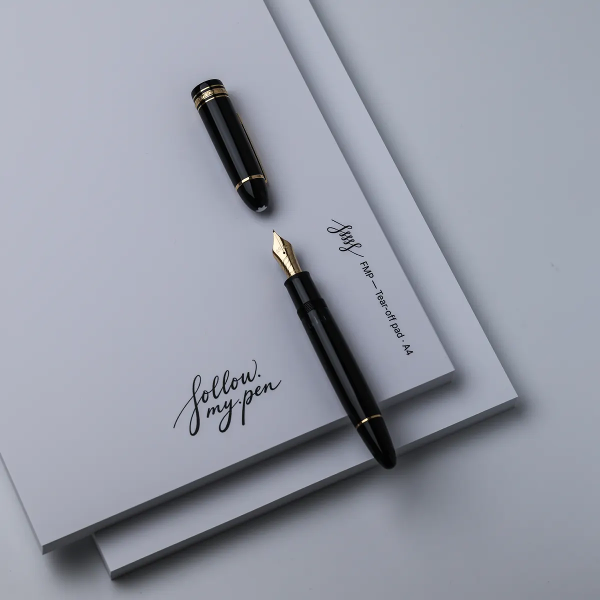 Uncapped black fountain pen with a gold nib on an FMP A4 tear-off pad, with its cap alongside