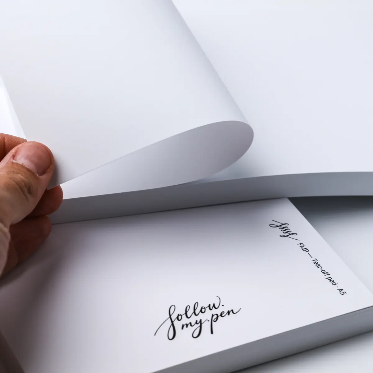 A hand lifting a blank white sheet from a tear-off pad above an FMP A5 branded cover