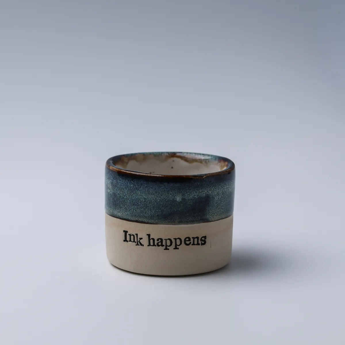 Front view of the Ink Happens mug with mottled blue glaze and black lettering