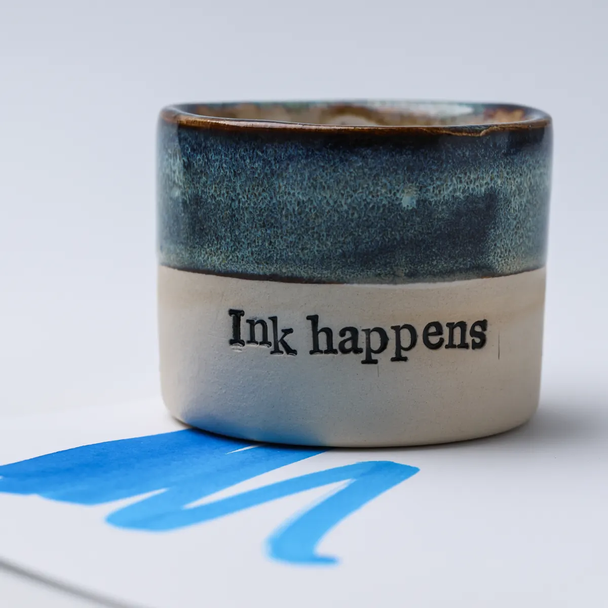 Close-up of the Ink Happens lettering and blue glaze with blue ink swatches in the foreground