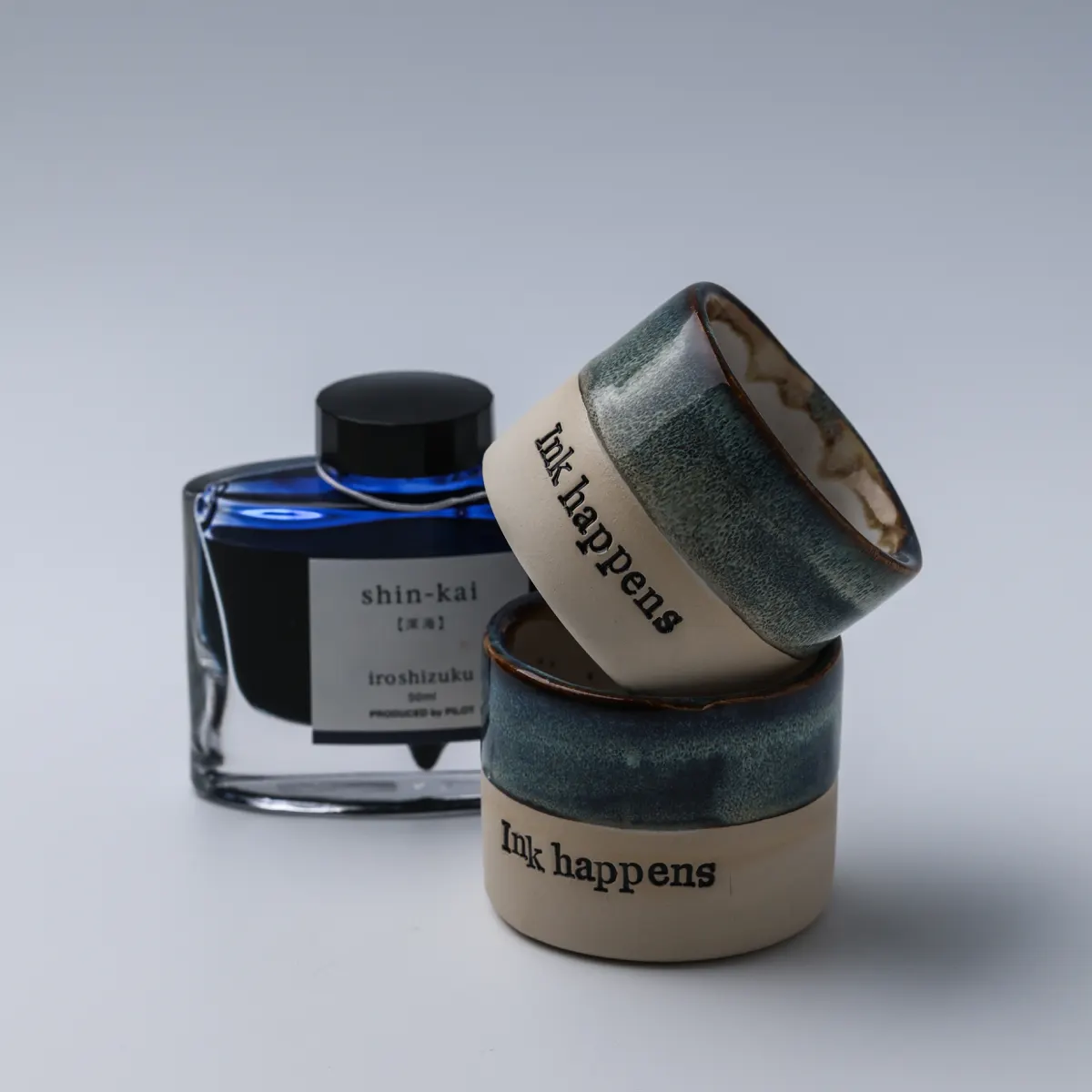 Two Ink Happens ceramic mugs stacked at an angle beside a fountain pen ink bottle