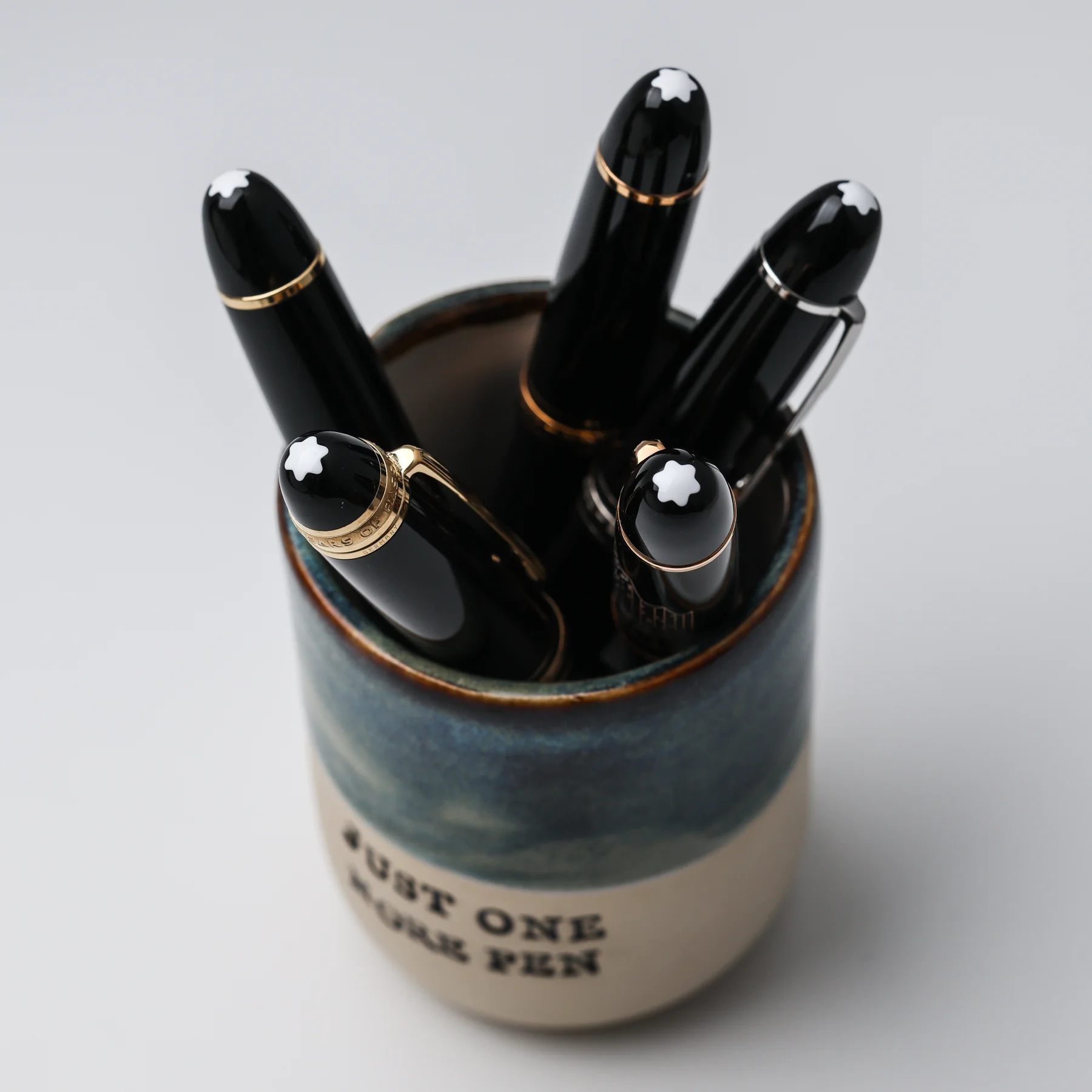 Overhead view of the Just One More Pen ceramic cup holding five black fountain pens, with its glazed rim visible